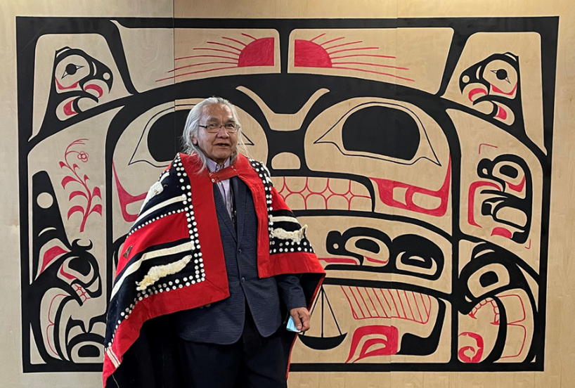Hazelton Indigenous Court art hanging on wall with artist Elder Art Wilson standing in front of it.