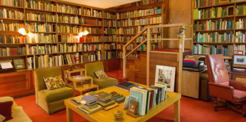 Author's study with chairs and table in foreground and shelves of books on the walls behind.