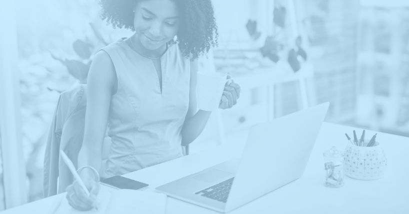 Woman sitting at desk taking notes with laptop in front of her.