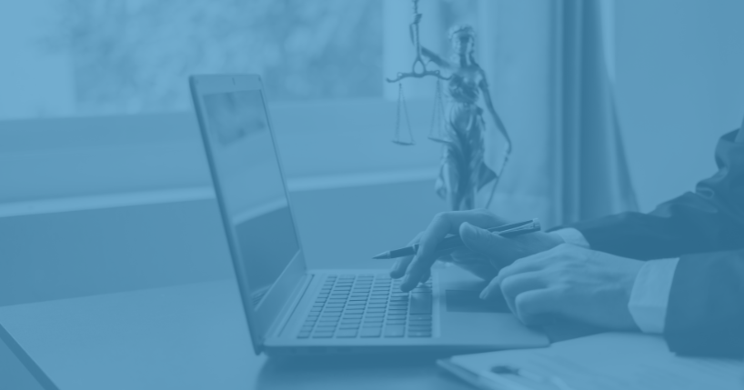 Man wearing business suit working at laptop with small statuette of lady justice next to him.